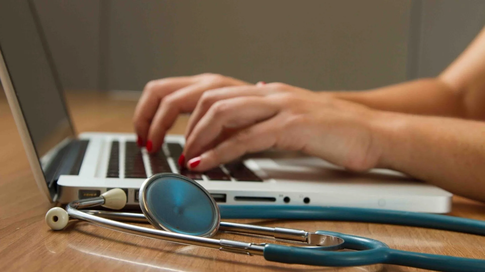 Una mujer escribiendo sobre el teclado de una computadora, a su lado tiene un estetoscopio