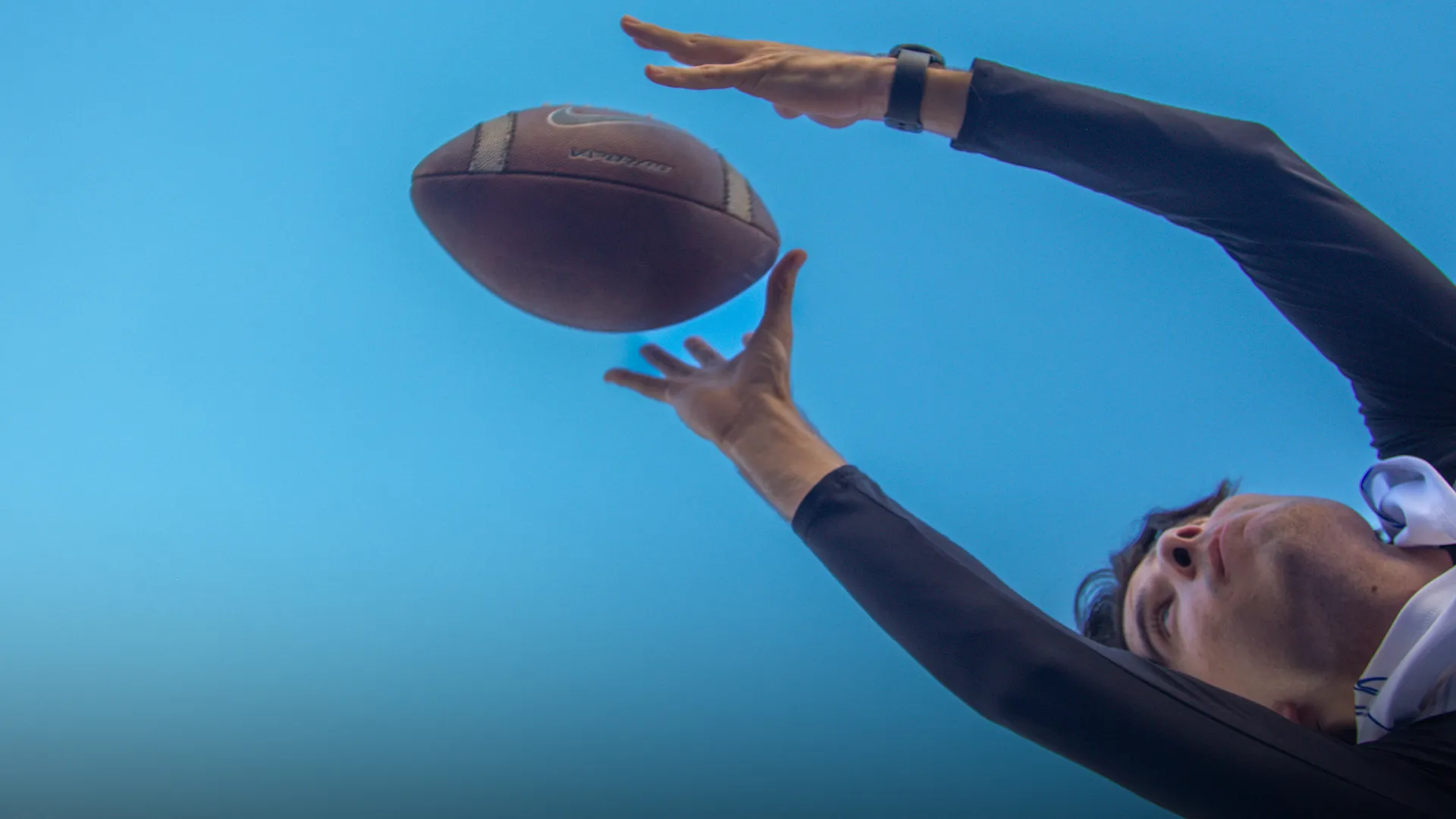 Vista desde el suelo de un juegador de flag football extendiendo los brazos para recibir el ovoide.