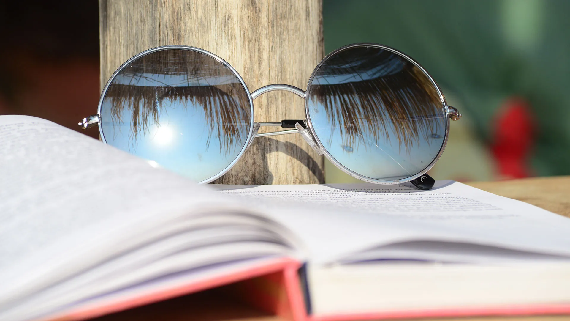 libro abierto y sobre éste, unos lentes de sol que reflejan palmeras