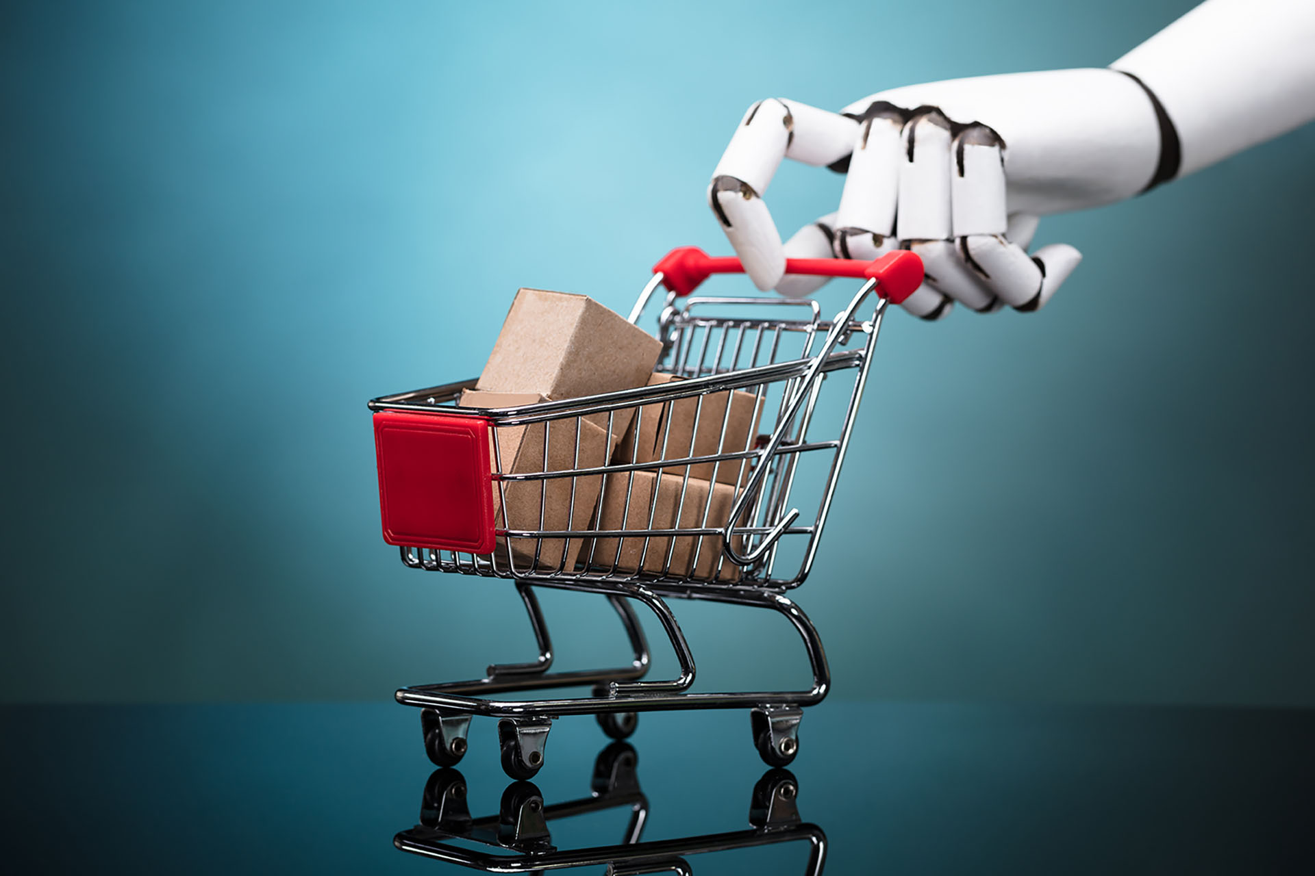 Robot sosteniendo un carrito de compras con cajas de cartón sobre fondo turquesa