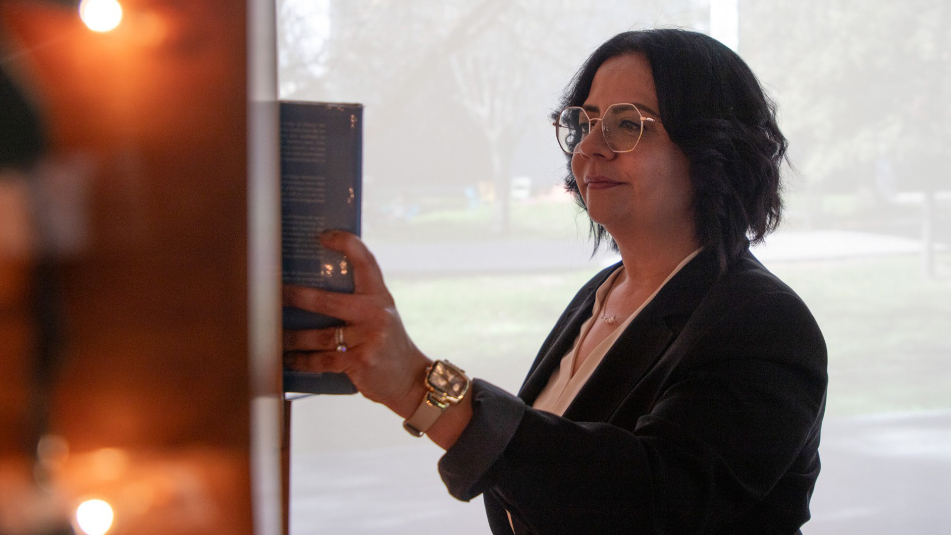 Directora de Mentoría de PrepaTec Laguna con vestimenta profesional toma libro de estante