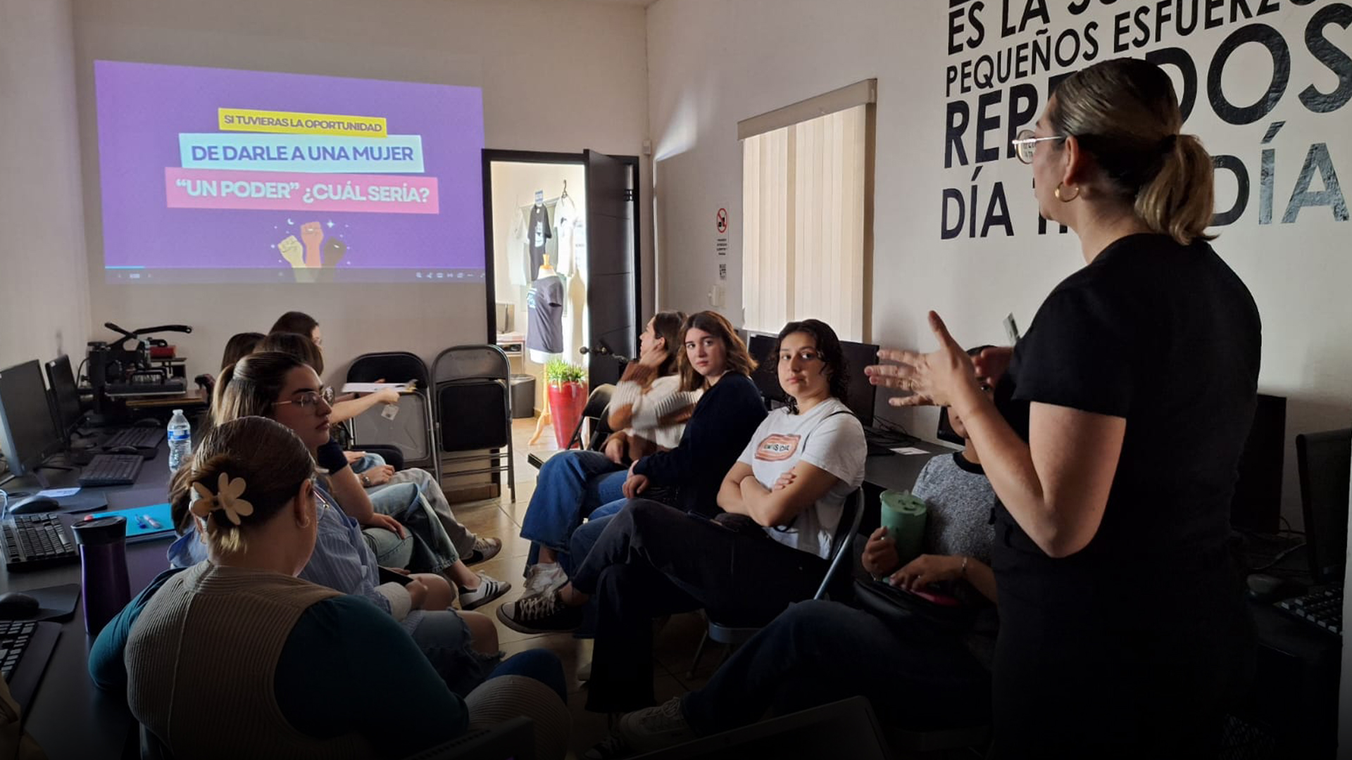 Mujer dando una platica frente a un grupo de mujeres jóvenes.