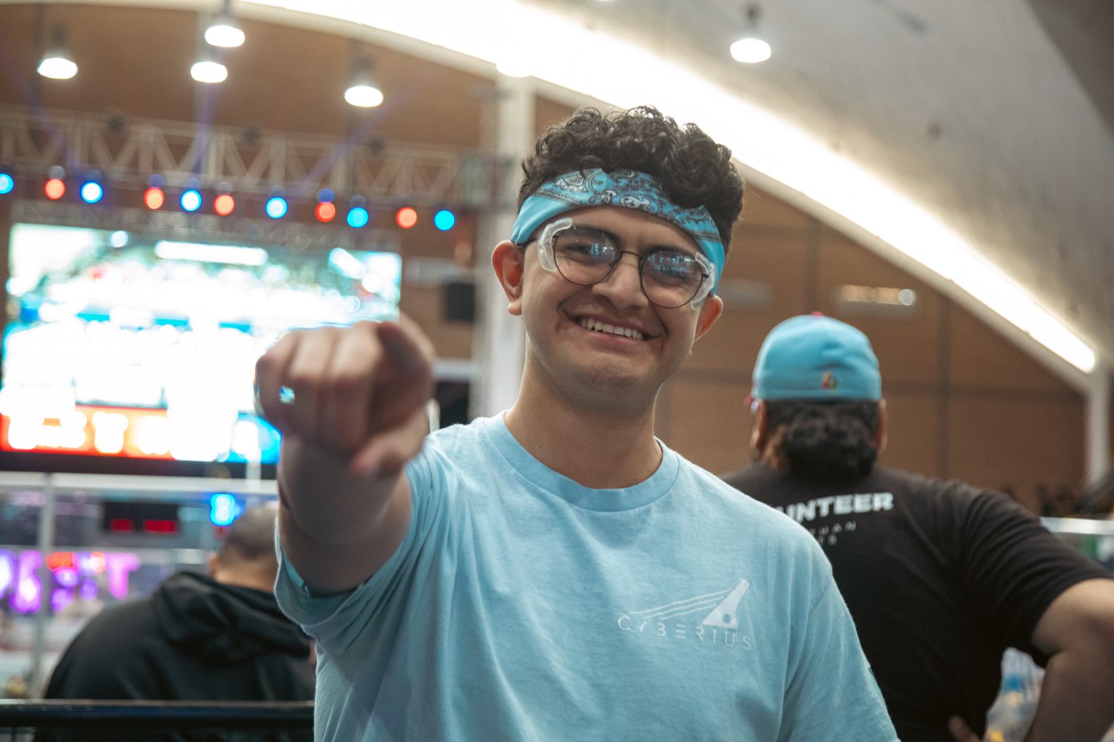 Pepe Santill&aacute;n se&ntilde;ala hacia la c&aacute;mara con la arena de FIRST Robotics Competition de fondo durante una competencia.