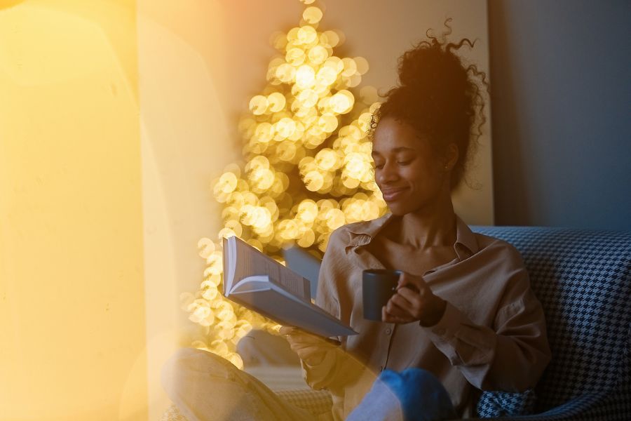 Joven leyendo un libro y tomando café cerca del árbol de Navidad en una acogedora sala de estar en casa