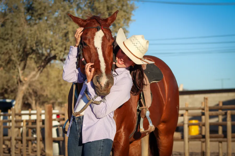 Chica abrazando la cabeza de un caballo sobre su hombro.