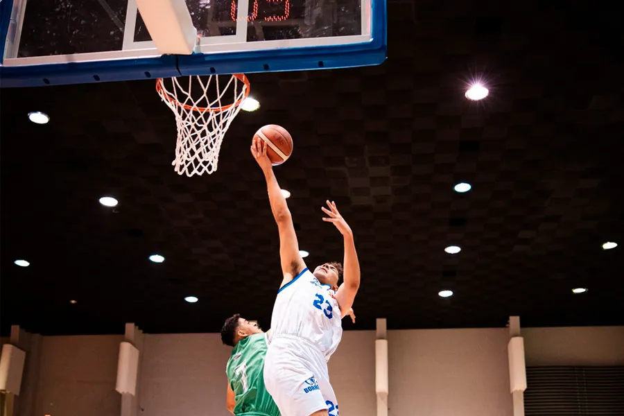 Jugador de Borregos Laguna está por encestar el balón de básquebtol ante la defensa de atleta vestido de verde