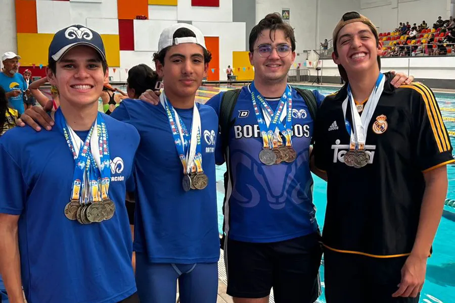 Cuatro jóvenes abarazados por los hombros vestidos con camisetas azules que dicen "Borregos" y múltiples medallas colagadas al cuello.