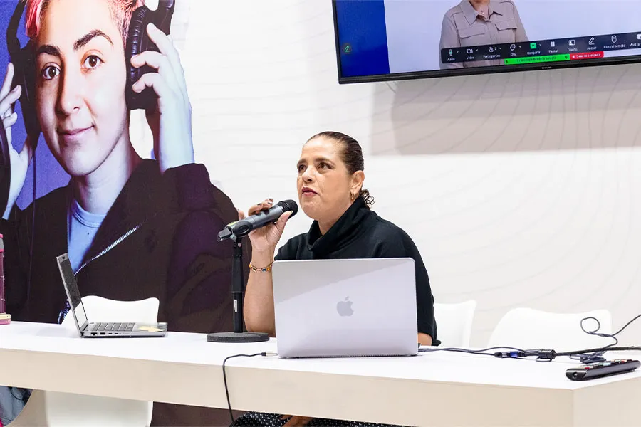 Muejer sentada en un escritorio hablando y sosteniendo un micr&oacute;fono.