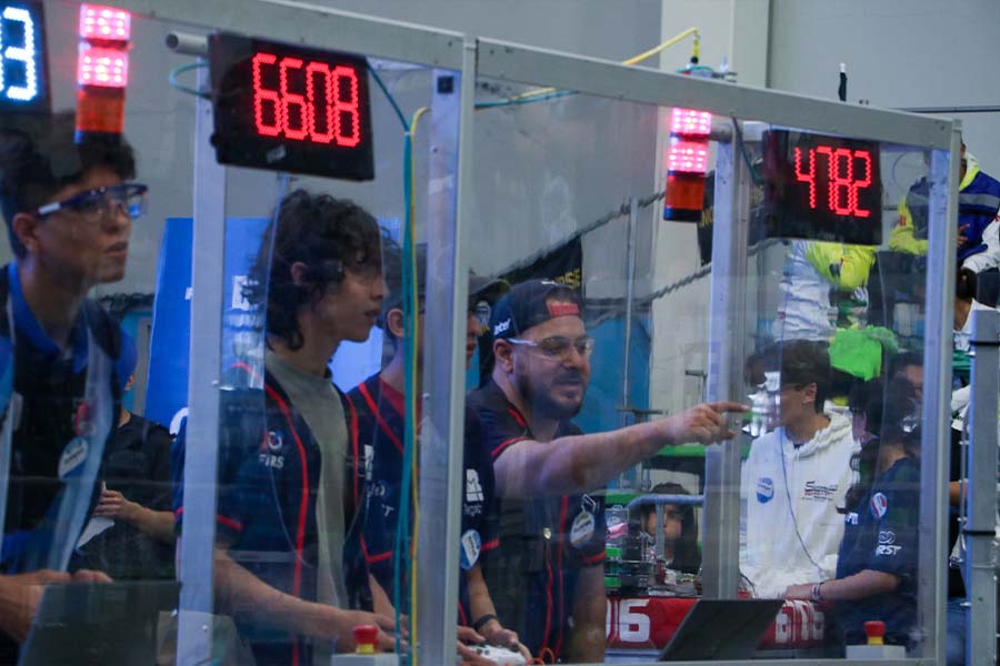 Dos alumnos y su coach detrás en la estación de manejo para controlar el robot durante la competencia.