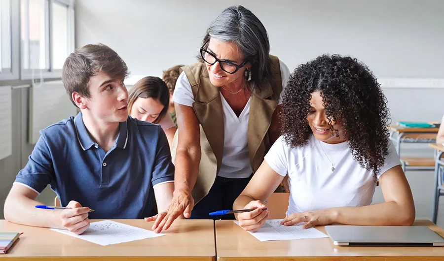 Profesora en salón de clases asesorando alumnos en su trabajo.