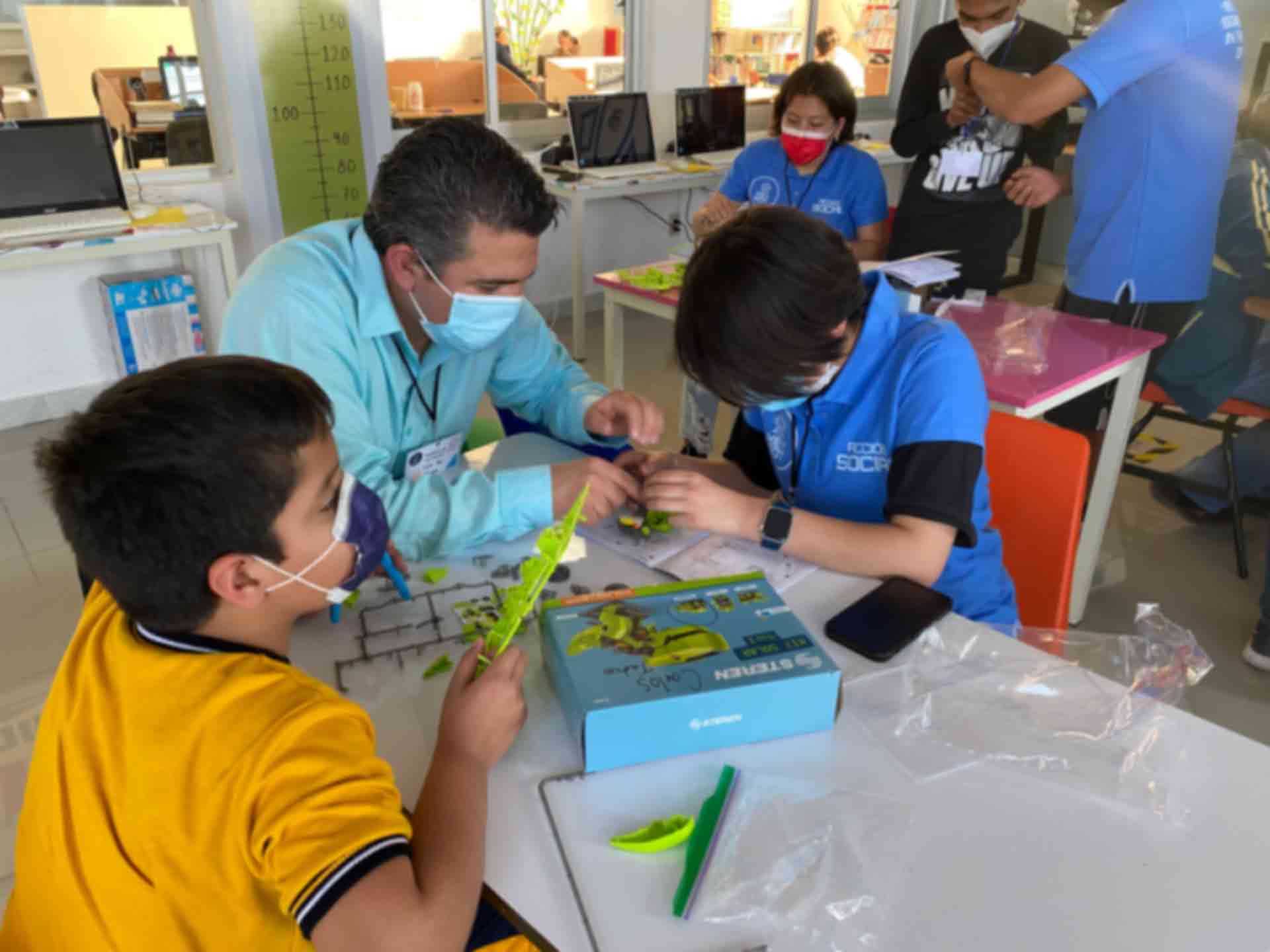 Niños construyendo robot con ayuda de un adulto