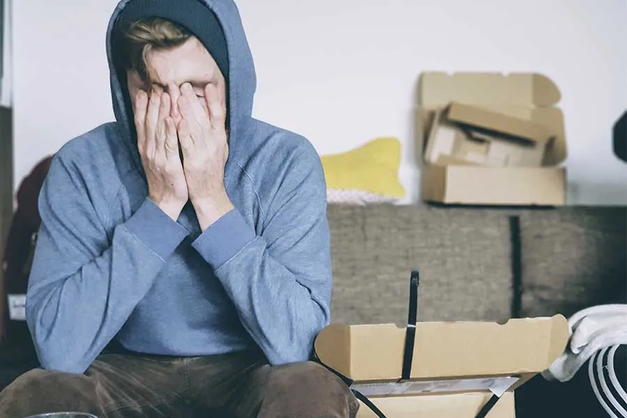 Joven con sudadera azul en un cuarto, con las manos en la cara y estresado