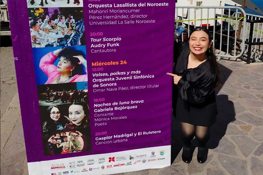 Mariana Páez posando junto a una lona donde se menciona su presentación dentro del FAOT.
