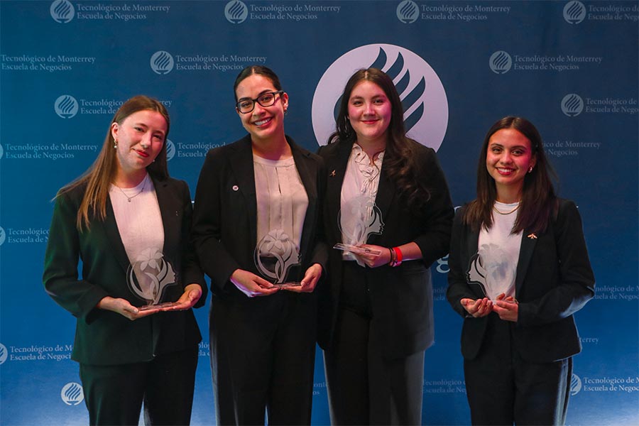 Cuatro estudiantes del Tecnológico de Monterrey sostienen sus premios en un evento de la Escuela de Negocios, posando frente a un fondo institucional.