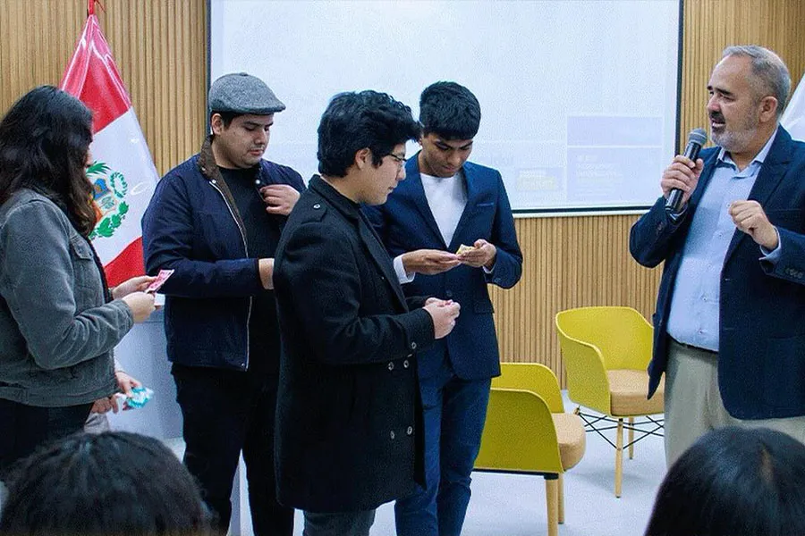 Profesor hablando con 4 alumnos al frente de un público.