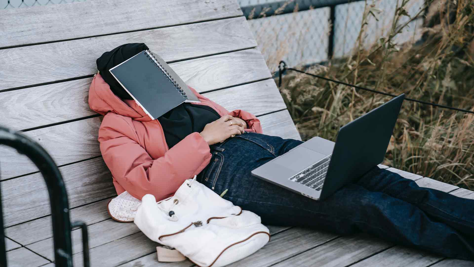 Estudiante dormido sobre banca con libreta sobre sus ojos