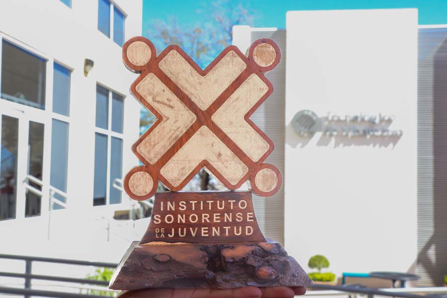 Trofeo con forma de X frente a una fachada del Tec de Monterrey.