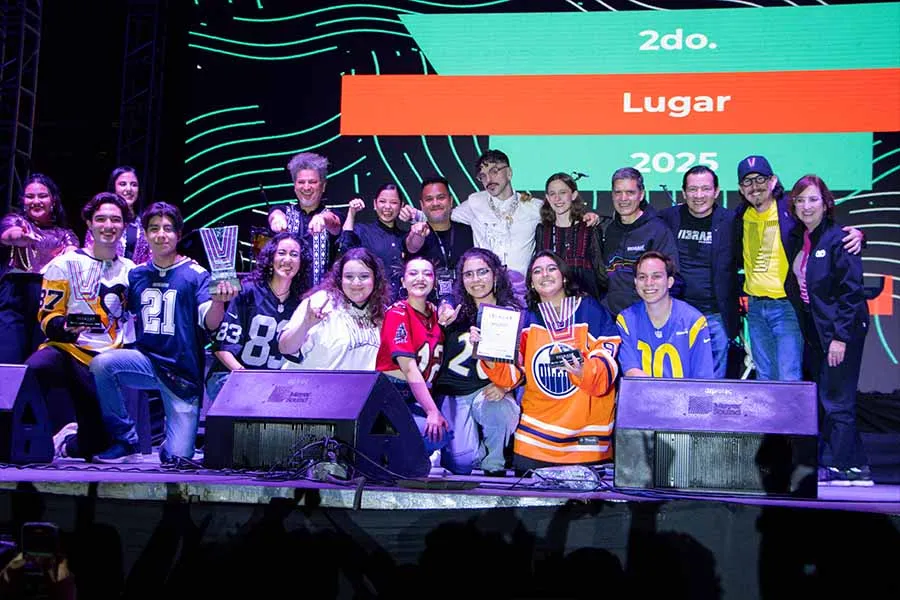 Banda de estudiantes posando con jurado y 4 trofeos sobre escenario. 
