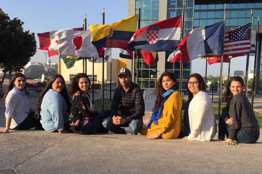 Estudiantes de profesional con ropa de frío posando para fotografía, de fondo banderas de distintos países.