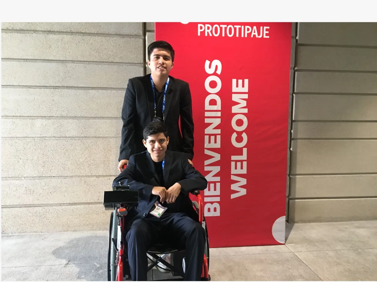 Daniel y Alexis con su prototipo de silla eléctrica frente a pancarta de congreso de prototipaje.