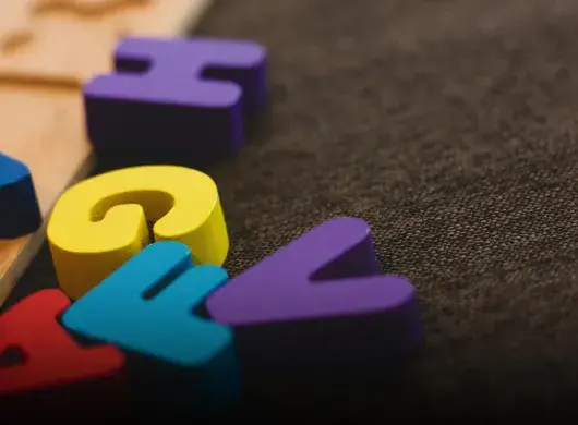 Letras coloridas de madera sobre alfombra oscura.