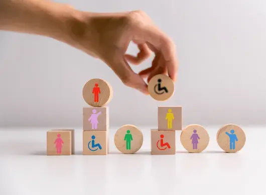 Mano acomoda bloques de madera con iconos que representan la diversidad de personas en la sociedad.
