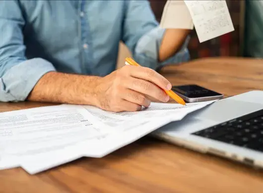 Hombre en camisa de mezclilla calculando impuestos con Comprobante y formas en un escritorio de madera. Concepto de preparación de impuestos y gestión financiera