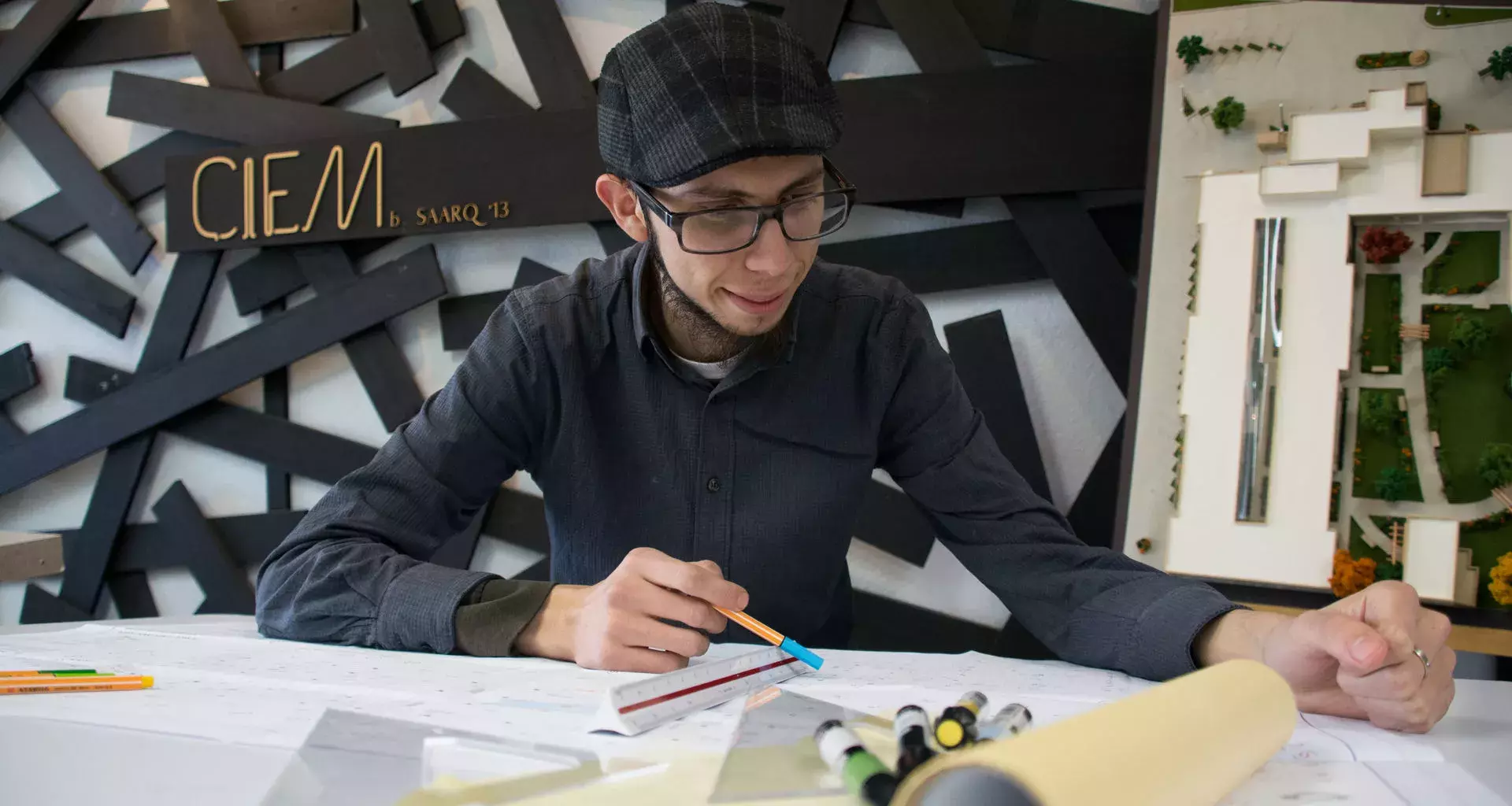 Jóven sonriente trabajando en una mesa con material de arquitectura alrededor 