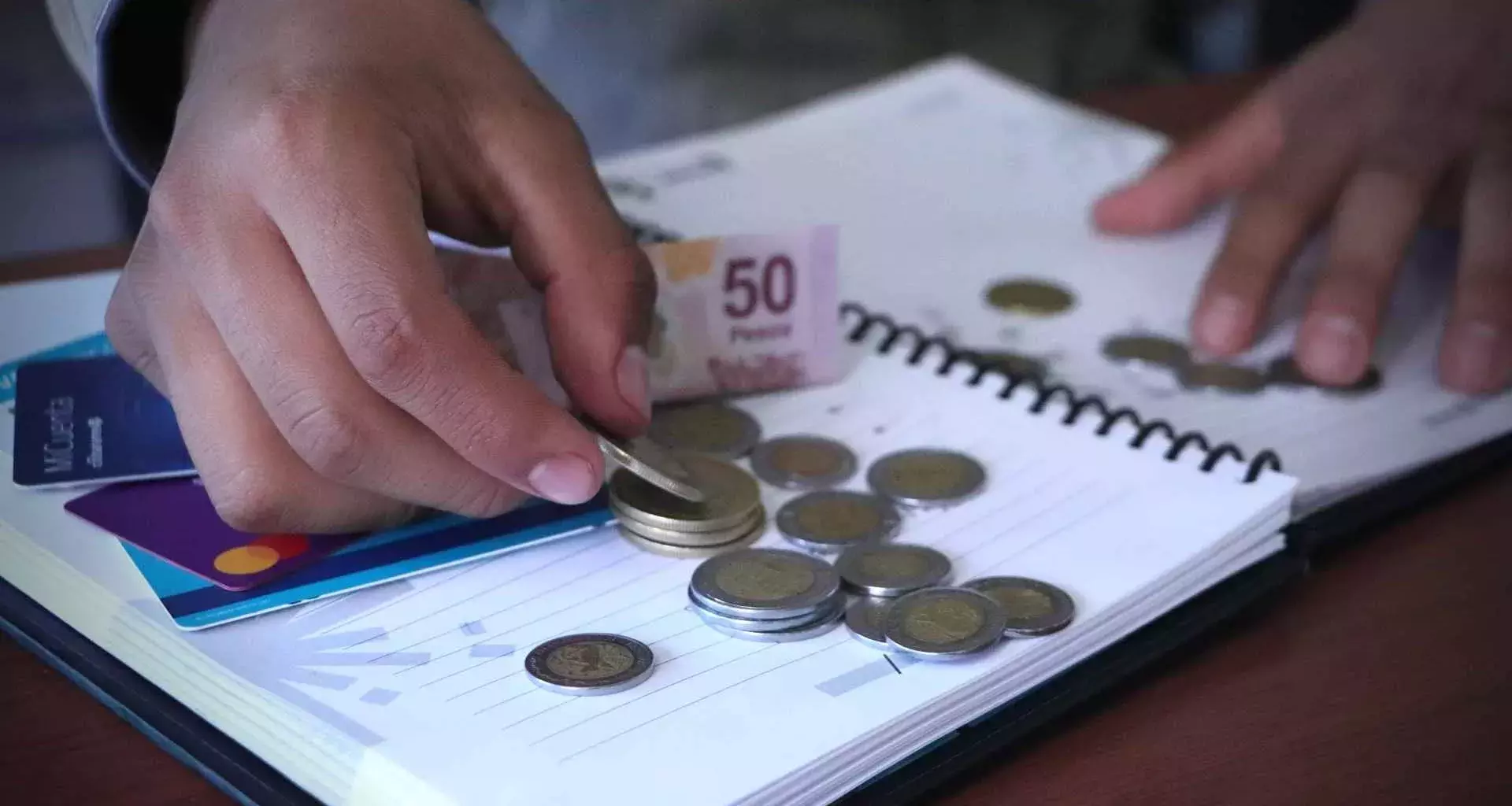 Persona cuenta dinero en escritorio con libreta y tarjetas bancarias