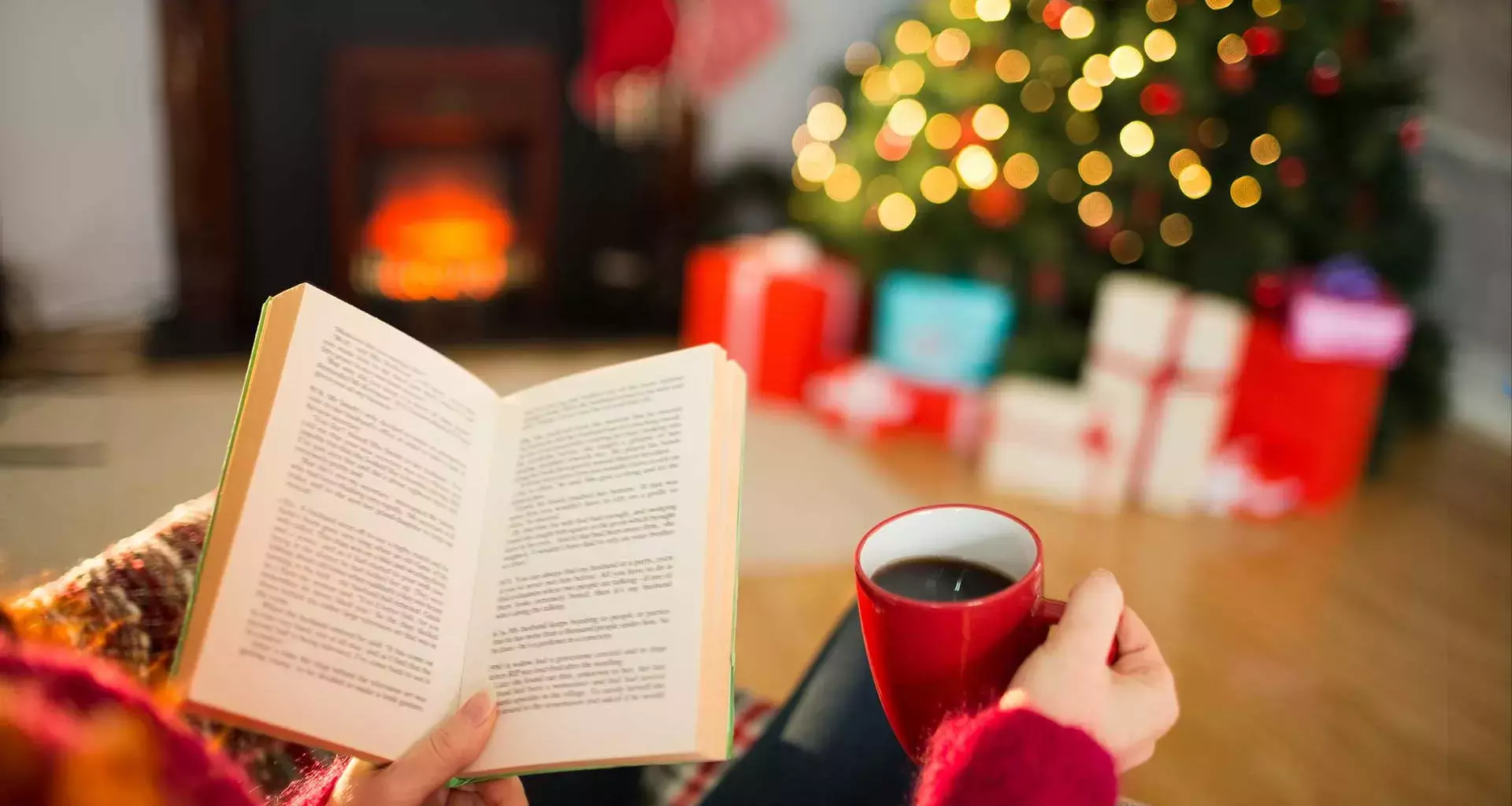 Mano de una mujer joven, sosteniendo un libro, y se observa al fondo el pino de navidad encendido