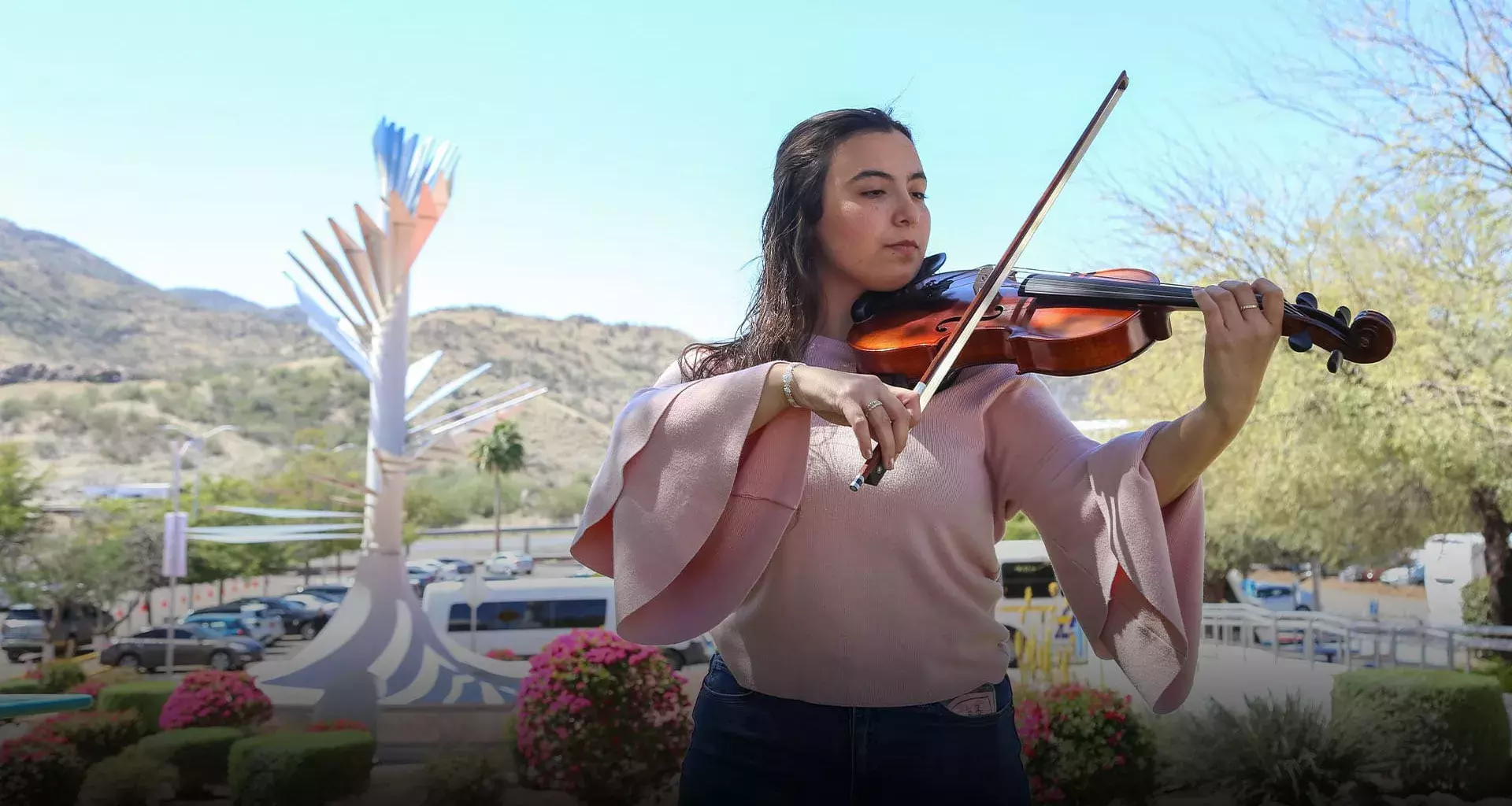 Mariana Páez tocando la viola frente a una vista de la Cápsula del Tiempo del campus Sonora Norte