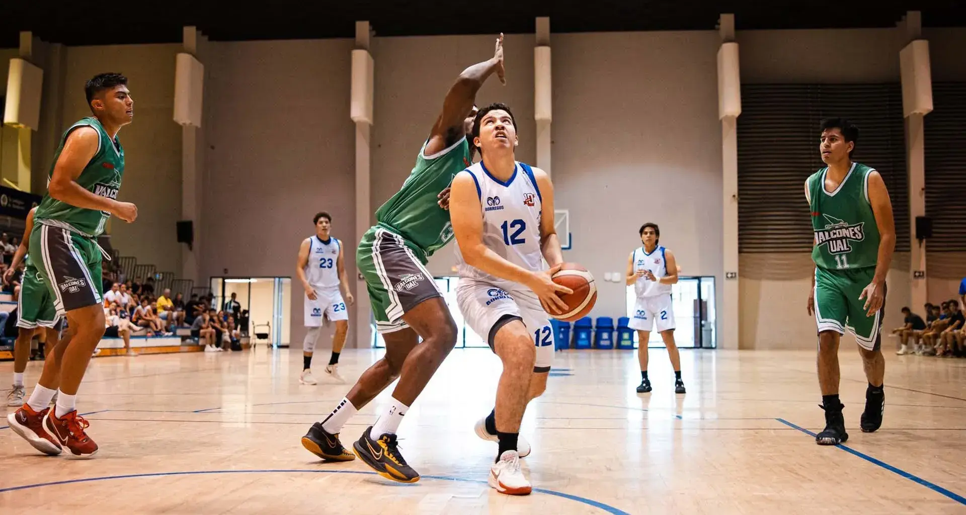 Jugador de Borregos Laguna con uniforme blanco disputa un enceste de básquetbol contra un atleta que viste jersey verde