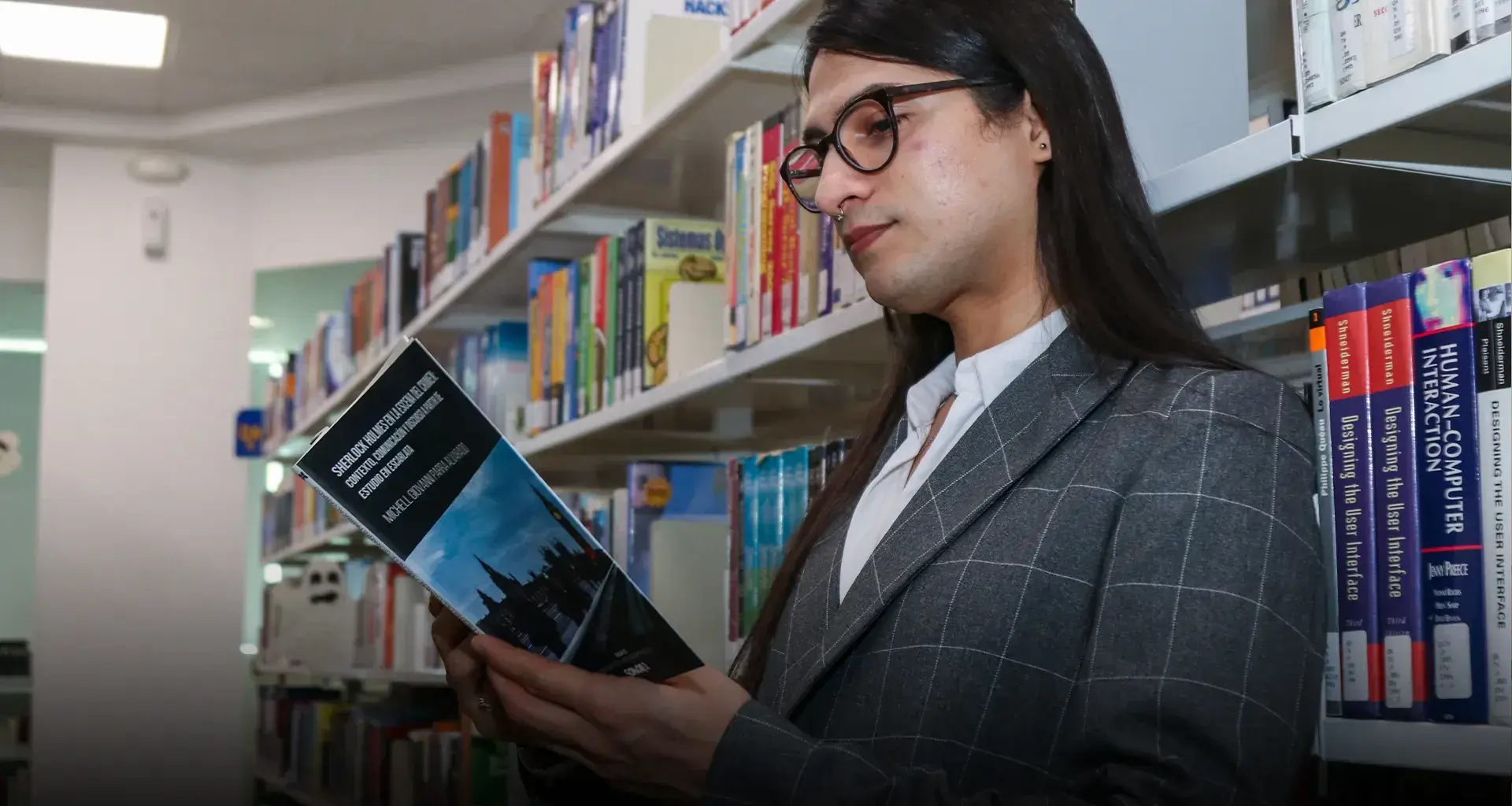 Profesor leyendo libro recargado contra un librero