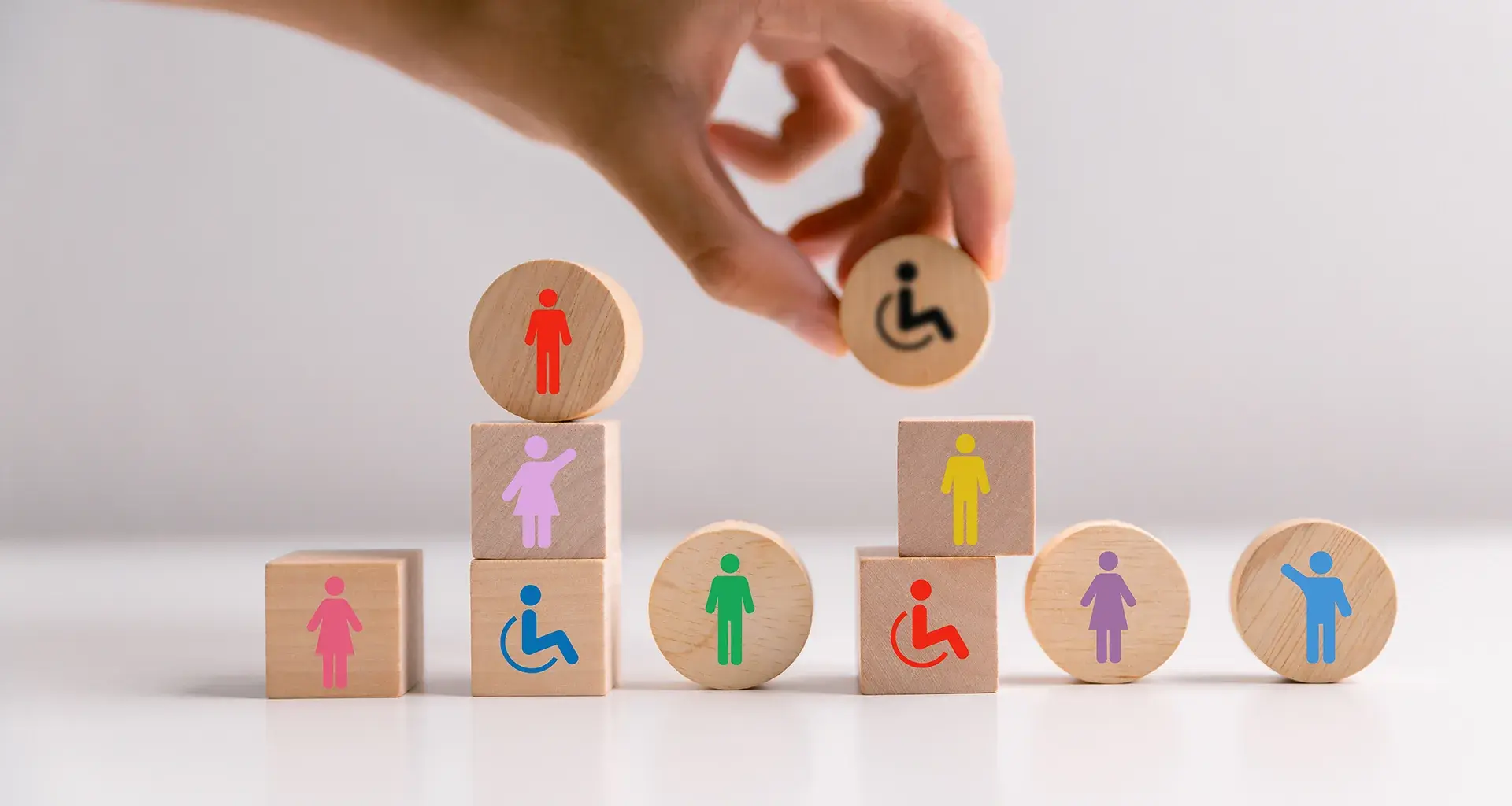 Mano acomoda bloques de madera con iconos que representan la diversidad de personas en la sociedad.