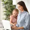 Madre de familia trabajando en su laptop, con su hija a una lado
