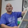 Profesor de artes plásticas pintando un cuadro con ligera sonrisa volteando hacia arriba.