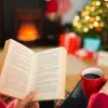 Mano de una mujer joven, sosteniendo un libro, y se observa al fondo el pino de navidad encendido