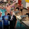 Montaje de alumnos 4 alumnos abrazados con múltiples medallas colgadas en los cuellos, sobre una foto de nadadores preparándose para iniciar una carrera.
