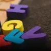 Letras coloridas de madera sobre alfombra oscura.