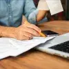 Hombre en camisa de mezclilla calculando impuestos con Comprobante y formas en un escritorio de madera. Concepto de preparación de impuestos y gestión financiera