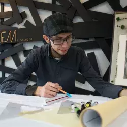 Jóven sonriente trabajando en una mesa con material de arquitectura alrededor 