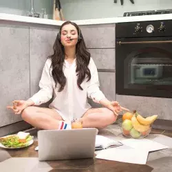 Joven con computadora, en posición de yoga y comida saludable alrededor, para representar el concepto de una rutina equilibrada