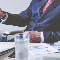 Hombre con traje azul marino, corbata roja, enfrente de una computadora