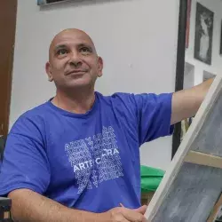 Profesor de artes plásticas pintando un cuadro con ligera sonrisa volteando hacia arriba.