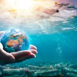 Imagen del mar contaminado con plástico, con una mano sosteniendo al mundo, conceptualizando el cuidado que requieren los océanos
