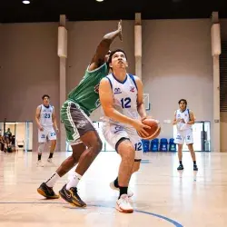 Jugador de Borregos Laguna con uniforme blanco disputa un enceste de básquetbol contra un atleta que viste jersey verde
