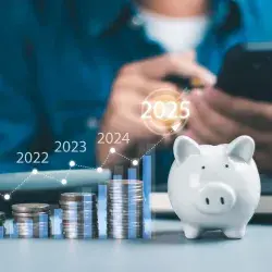 Foto conceptual de una persona calculando sus finanzas, y al frente una alcancía con monedas a lado