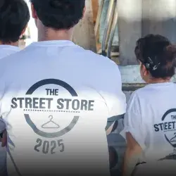 Vista de espaldas de tres voluntarios portando camisetas blancas con un logo que dice Street Store 2025