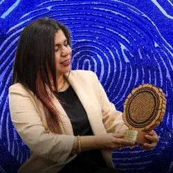 Mujer con saco blanco sosteniendo trofeo con forma de corte transversal de tronco y mirando hacia el.