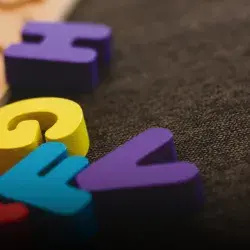 Letras coloridas de madera sobre alfombra oscura.